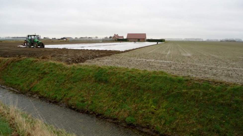 Johan Fase trekt plastic over de aardappelen die hij net heeft gepoot.